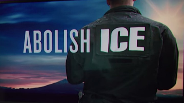 "Abolish ICE across a twilight image and ICE agent, back turned to viewer